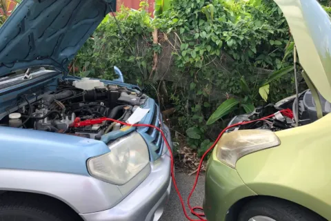 Seorang pengemudi sedang memeriksa mesin untuk mengatasi mobil sulit dinyalakan di pinggir jalan