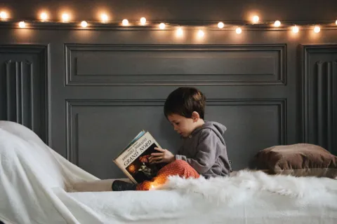 Orang tua membacakan buku cerita bergambar bersama anak di atas karpet rumah untuk membangun kebiasaan membaca sejak dini