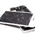 Tangan memegang smartphone dengan layar retak halus yang dipasangi pelindung kaca