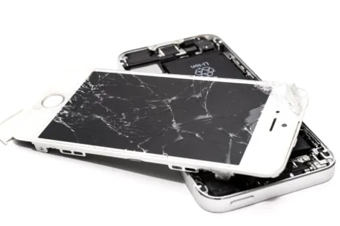 Tangan memegang smartphone dengan layar retak halus yang dipasangi pelindung kaca