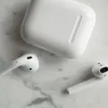 Seseorang sedang memegang sepasang earphone tanpa kabel berwarna putih di samping wadah pengisi daya
