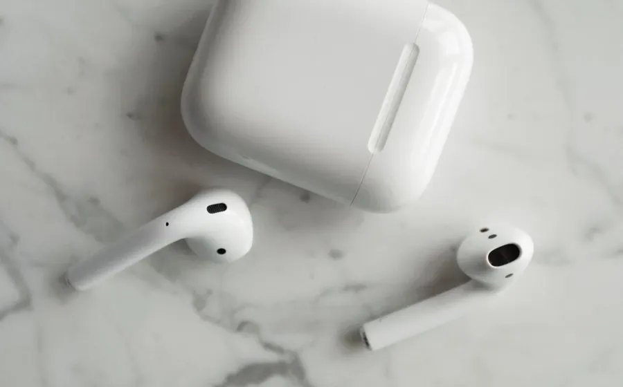 Seseorang sedang memegang sepasang earphone tanpa kabel berwarna putih di samping wadah pengisi daya
